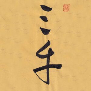 Two Chinese characters San Cai rendered in expressive cursive script calligraphy on warm ochre textured paper with a red seal stamp at the top right.