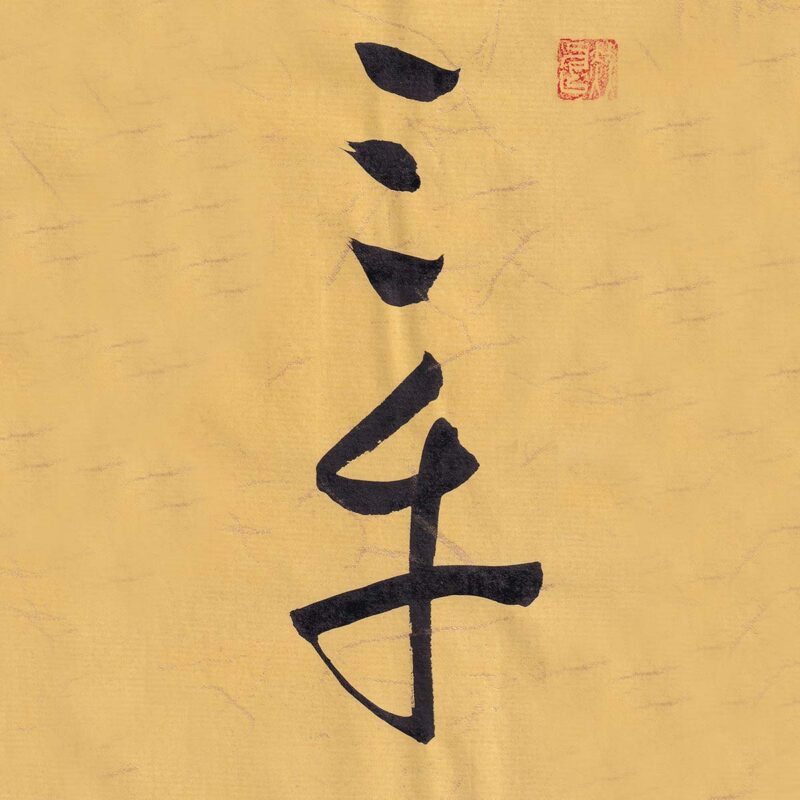 Two Chinese characters San Cai rendered in expressive cursive script calligraphy on warm ochre textured paper with a red seal stamp at the top right.