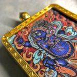 Close-up of blue Acala Fudo Myoo pendant in brass Gau box with flame background.