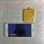 Size comparison of Amitabha Gau box pendant shown next to a smartphone.