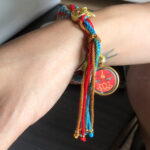 Red Amitayus Buddha Eyes charm bracelet worn on wrist for spiritual protection.