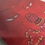 Macro detail of hand-painted gold linework on Amitayus Buddha Eyes red canvas.