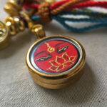 Close-up of Amitayus Buddha Eyes red charm with hand-painted gold linework.