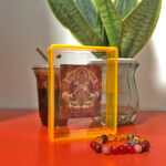 Red Amitayus Thangka yellow acrylic art block styled next to prayer beads on a red desk.