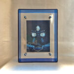 Front view of Black Jambhala Buddha Eyes print in a blue floating translucent acrylic frame.