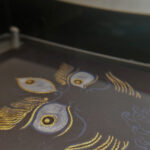 Close-up of original hand-painted gold linework and wrathful wisdom eyes on dark canvas texture.