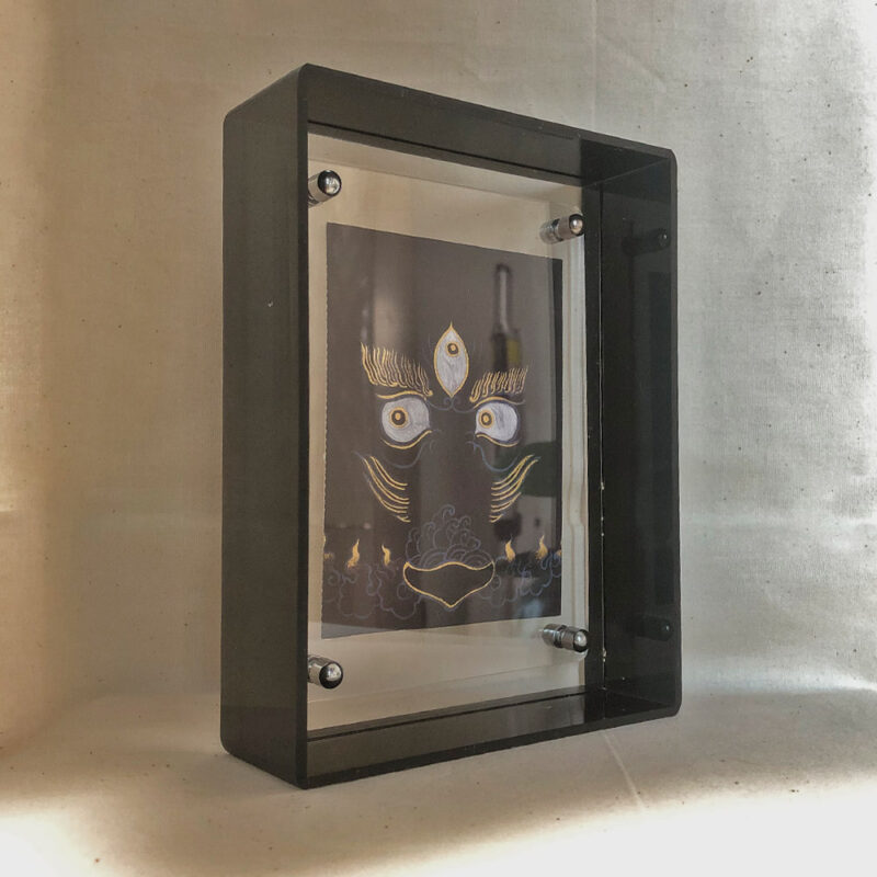 Side perspective of Black Jambhala Buddha Eyes art inside a black translucent acrylic frame.