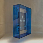 Side perspective of Black Jambhala Buddha Eyes art inside a blue translucent acrylic frame.