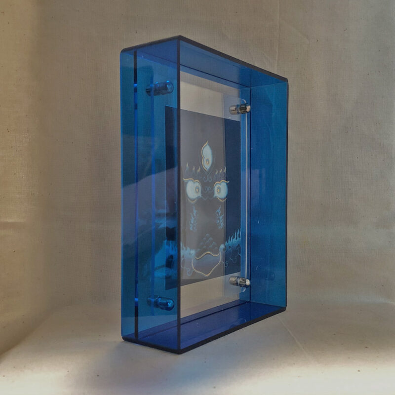 Side perspective of Black Jambhala Buddha Eyes art inside a blue translucent acrylic frame.