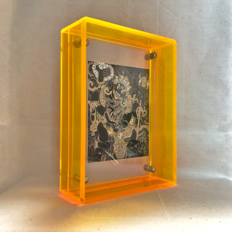 Side perspective of Black Jambhala Thangka print inside a yellow translucent acrylic display frame.