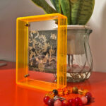 Black Jambhala Thangka in a yellow translucent acrylic frame styled on a desk with prayer beads.