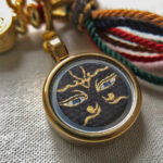 Close-up view of Black Padmasambhava Buddha Eyes artwork with hand-applied gold linework in a Ghau box pendant.