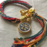 Angled view of Black Padmasambhava Buddha Eyes Ghau pendant attached to colorful braided cord.