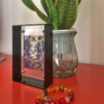 Clear acrylic thangka desk display styled next to a green plant on a red table.