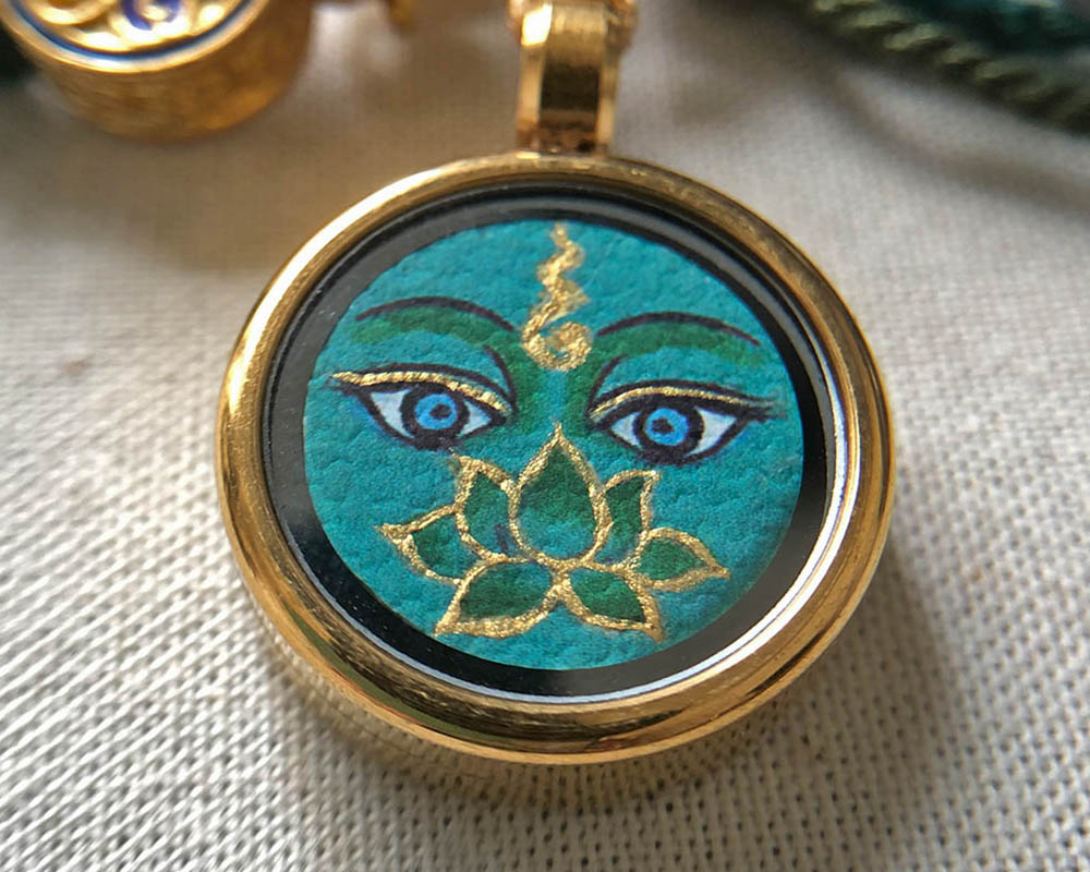 Text: Close-up detail of a 1.5cm circular Buddha Eye miniature painting with green background and gold lotus