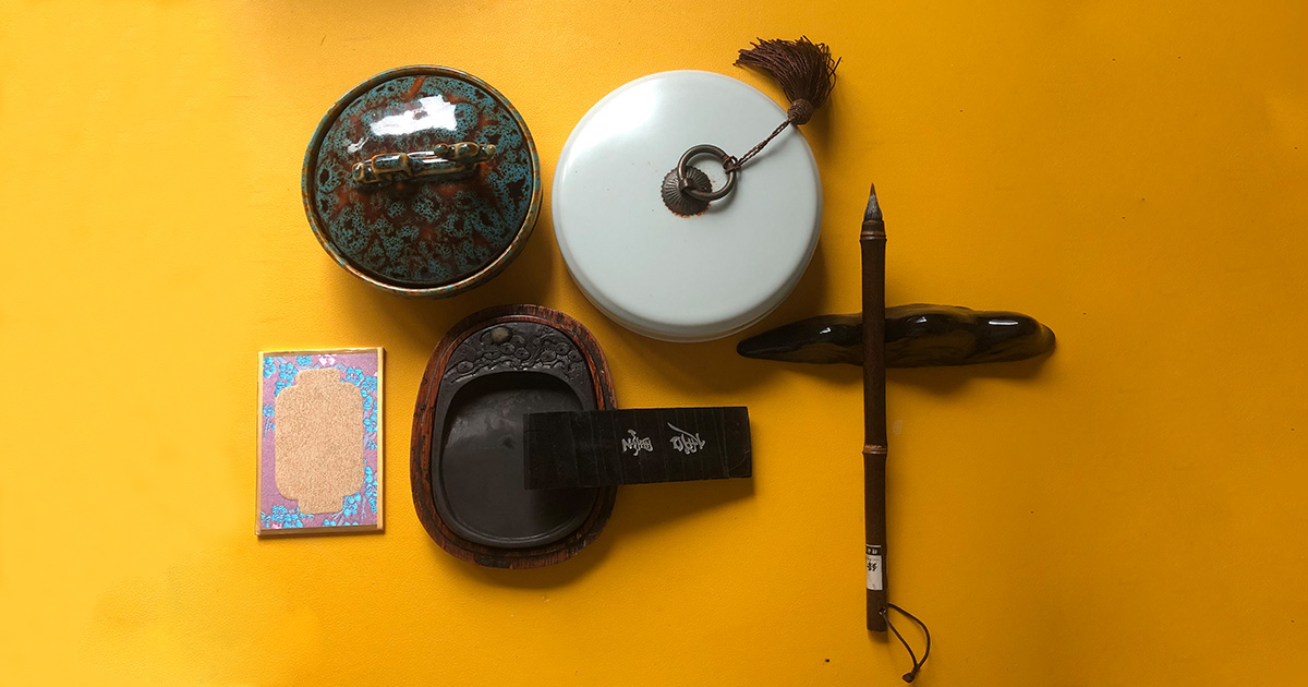 Traditional Chinese calligraphy tools four treasures including brush inkstone and seals on yellow background