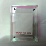 Back view of clear acrylic frame displaying Golden Ink Arts custom branding card.