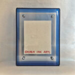 Back view of blue acrylic frame displaying Golden Ink Arts custom branding card.