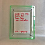 Back view of green acrylic frame displaying Golden Ink Arts custom branding card and signature.