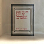 Back view of black acrylic frame displaying Golden Ink Arts custom branding card and signature.