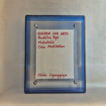 Back view of blue acrylic frame displaying Golden Ink Arts custom branding card and artist signature.