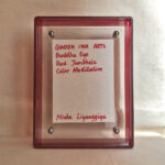 Back view of red acrylic frame displaying Golden Ink Arts custom branding card and signature.