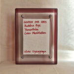 Back view of red acrylic frame displaying Golden Ink Arts custom branding card and artist signature.