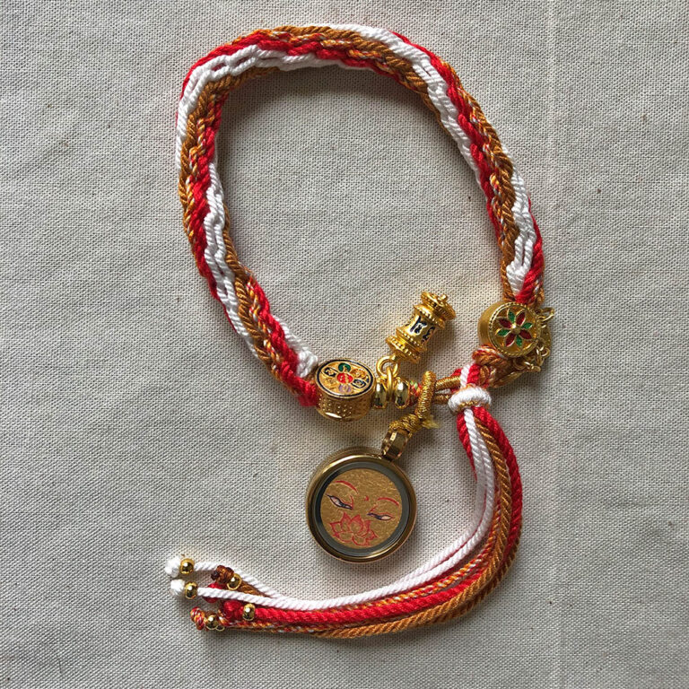 Golden Shakyamuni Buddha Eyes Tibetan braided meditation bracelet flatlay on fabric.