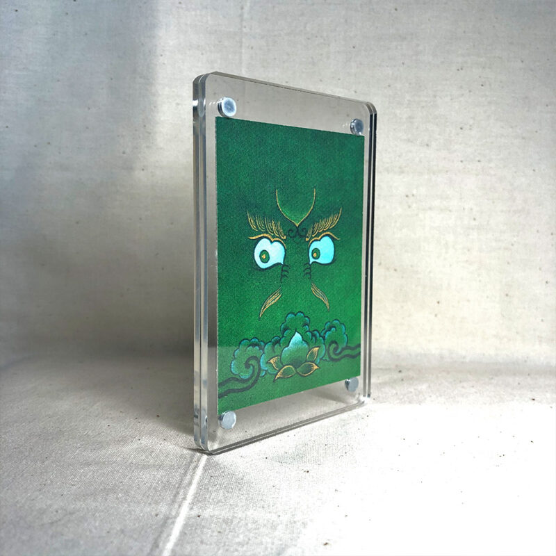 Side-angle view of freestanding clear acrylic block displaying Green Jambhala line art.