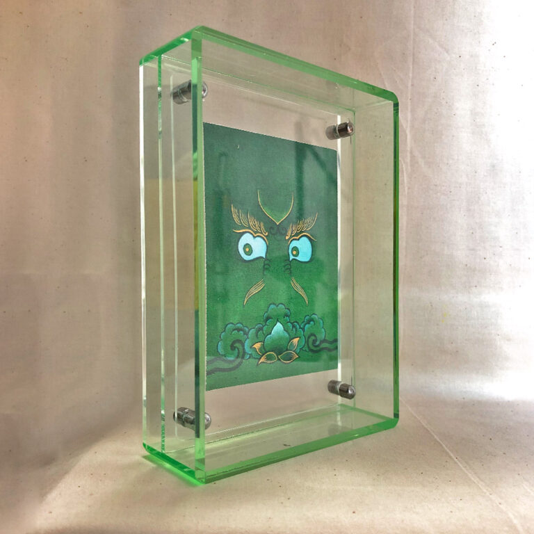 Side perspective of Green Jambhala Buddha Eyes art inside a green translucent acrylic frame.