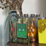 Green Jambhala Buddha Eyes Thangka in a green translucent acrylic frame styled on a shelf with glass bottles.
