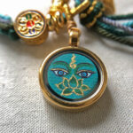 Close-up of Green Tara Buddha Eyes green charm with hand-painted gold linework.