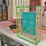 Green Tara Buddha Eyes Thangka in a green translucent acrylic frame styled on a desk shelf.