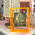 Green Tara Thangka in a yellow translucent acrylic frame styled on a desk in a serene home setting.