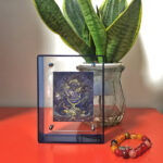 Indigo Black Jambhala Thangka in a blue translucent acrylic frame styled on a desk with prayer beads.