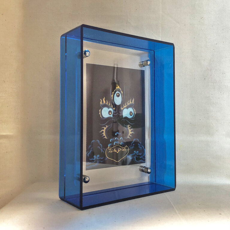 Side perspective of indigo Mahakala Buddha Eyes art inside a blue translucent acrylic frame.
