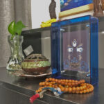 Indigo Mahakala Buddha Eyes Thangka in a blue translucent acrylic frame styled on a desk with prayer beads.