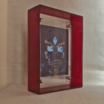 Side perspective of indigo Yamantaka Buddha Eyes art inside a red translucent acrylic frame.