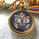 Close-up of Mahakala indigo Buddha Eyes charm with hand-painted gold linework.
