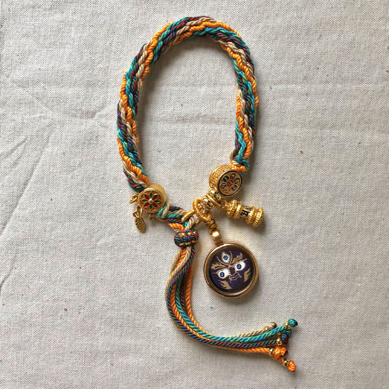 Vertical layout of the indigo Mahakala Buddha Eyes charm bracelet with woven cord.