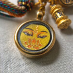 Close-up of Manjushri Buddha Eyes yellow charm with hand-painted gold linework.