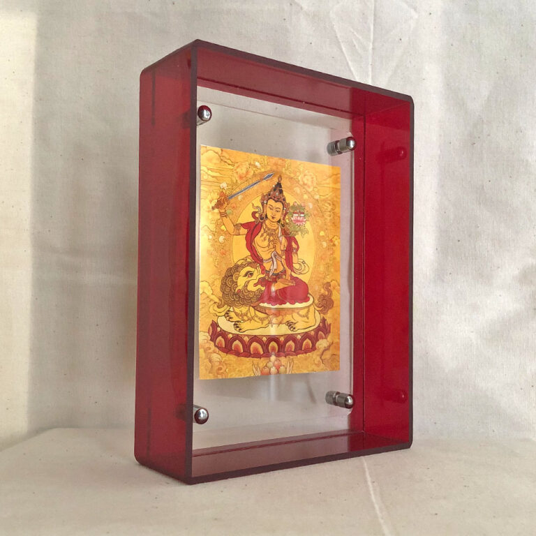 Side view of golden Manjushri Thangka art print inside a thick red acrylic display frame.