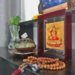 Golden Manjushri Thangka red acrylic art block styled next to prayer beads on a desk.