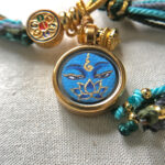 Close-up of Medicine Buddha Eyes blue charm with hand-painted gold linework.