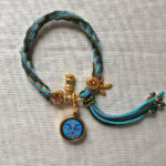Full view of blue Medicine Buddha Eyes pendant and braided cord.