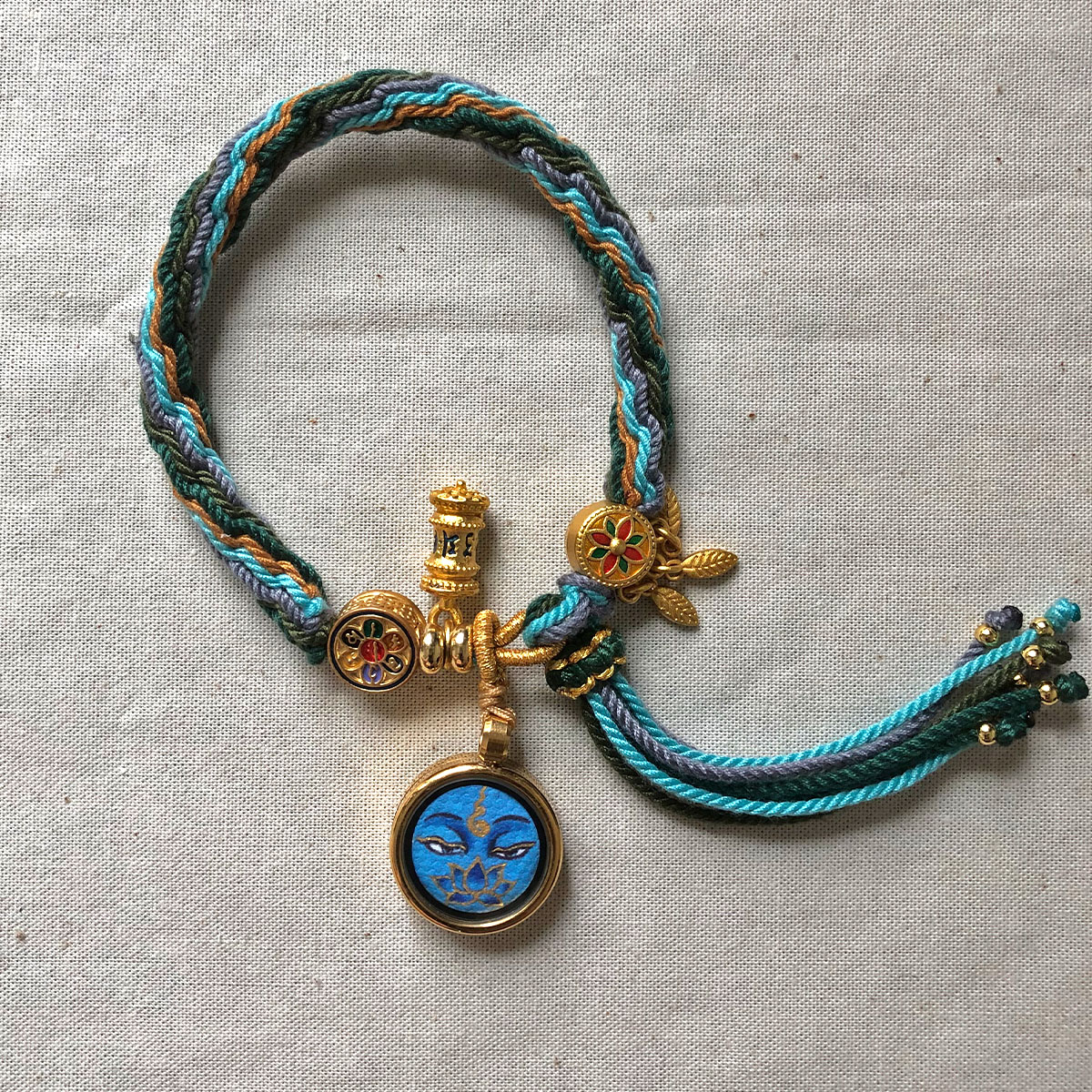 medicine-buddha-eyes-sacred-charm-woven-cord-pendant Full view of blue Medicine Buddha Eyes pendant and braided cord.