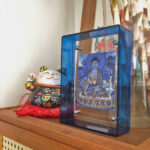 Medicine Buddha Thangka in a blue translucent acrylic frame styled on a desk with a fortune cat.