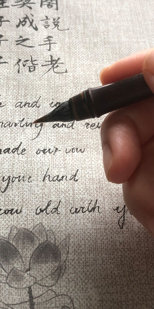 Hand holding a Chinese calligraphy brush writing classic characters on xuan paper
