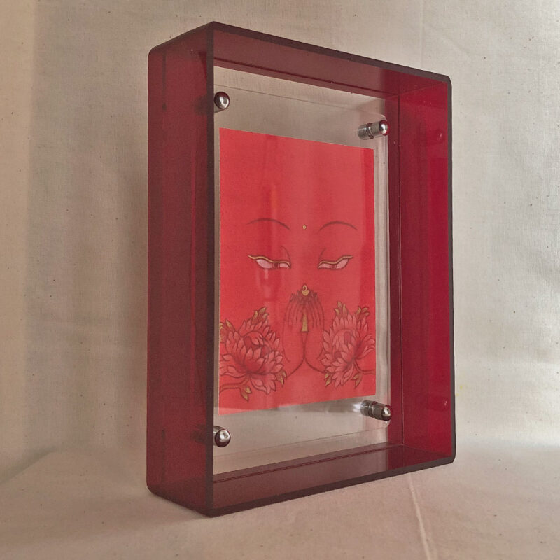 Side perspective of orange Avalokiteshvara Buddha Eyes art inside a red translucent acrylic frame.