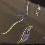 Close-up of original hand-painted gold linework and wisdom eyes on black canvas texture.